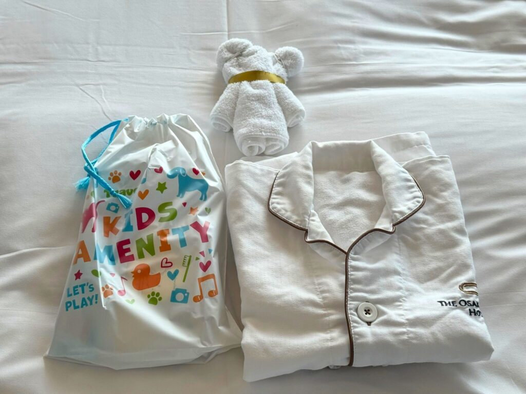 大阪ステーションホテルの子ども用アメニティ。パジャマと専用のアメニティ袋、タオルアートのクマがベッドの上に用意されている。