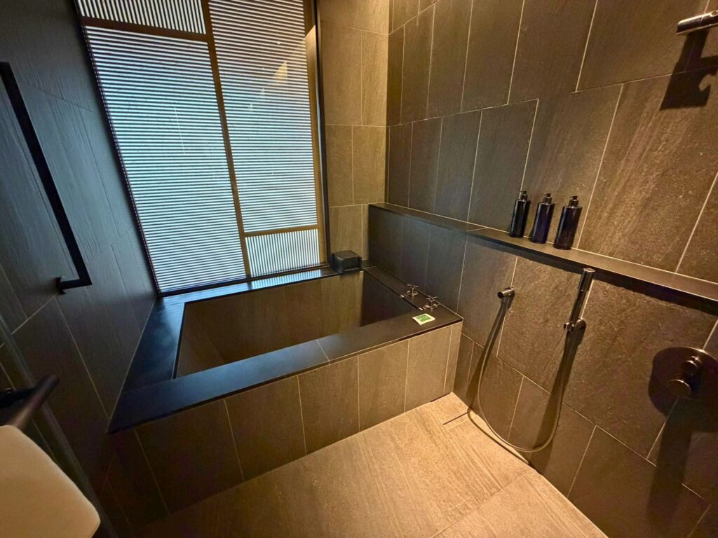 ROKU京都の浴室。黒を基調としたシックなデザインで、広々とした浴槽とシャワーを備える。