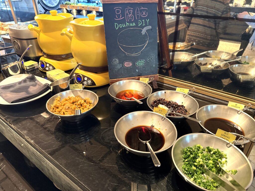 W蘇州ホテルの朝食ビュッフェの豆花DIYコーナー。黄色いポットでの豆花に好みのトッピング(黒豆・生姜シロップ・ネギ等)をかけて楽しめる中国伝統スイーツ