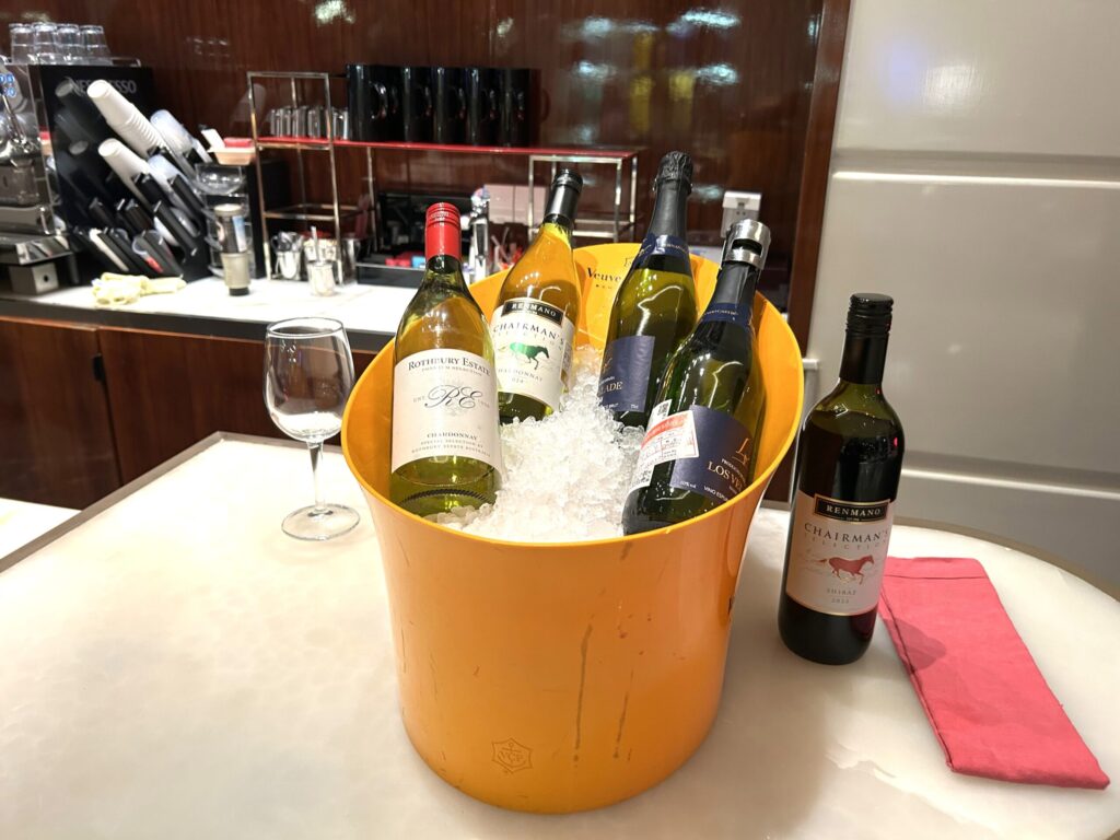 W蘇州ホテルのハッピーアワー。オレンジ色のアイスバケツにシャルドネ・シャンパンなど複数のワインボトルが冷やされ、グラスと赤ワインが添えられている