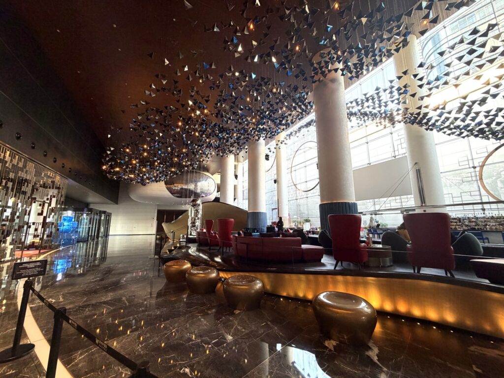 W蘇州ホテルのロビー。天井に無数の黒い三角形のアートインスタレーションが吊るされ、光沢のある大理石の床と深紅のソファが並ぶ開放的な空間