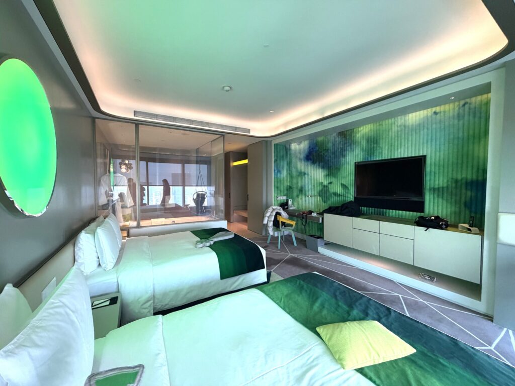 W蘇州ホテルのツインルーム全景。グリーンのLED照明に照らされた2台のベッド、水墨画風のアート壁面とテレビが並ぶスタイリッシュな空間